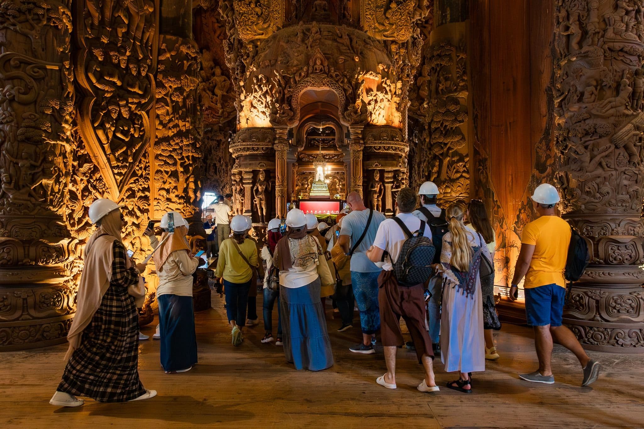 Visitors explore the richly carved wooden interior of the Sanctuary of Truth in Pattaya.