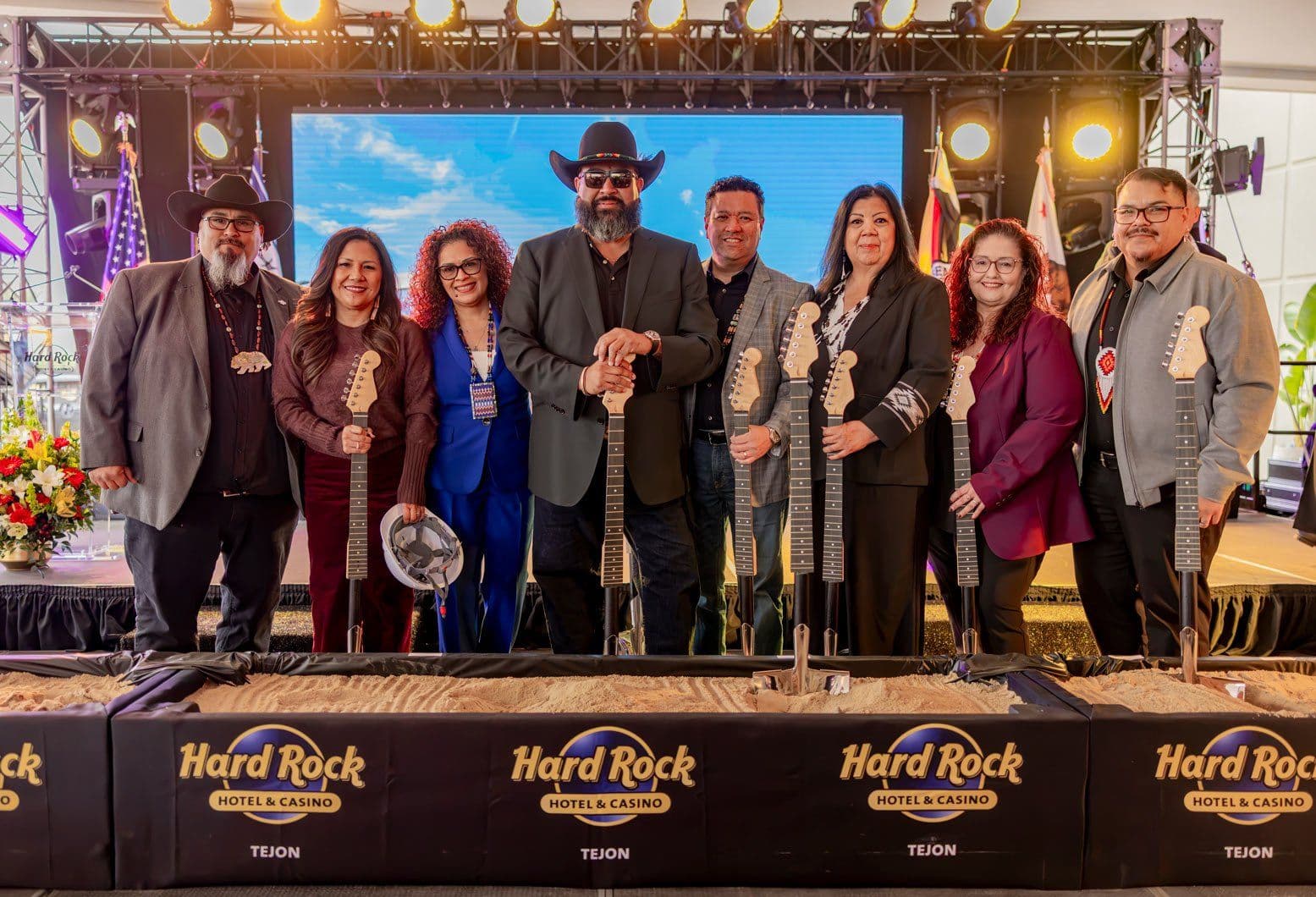 Tejon Indian Tribe leaders and Hard Rock representatives holding guitar-shaped shovels behind a sand-filled Hard Rock Hotel & Casino Tejon box at the groundbreaking